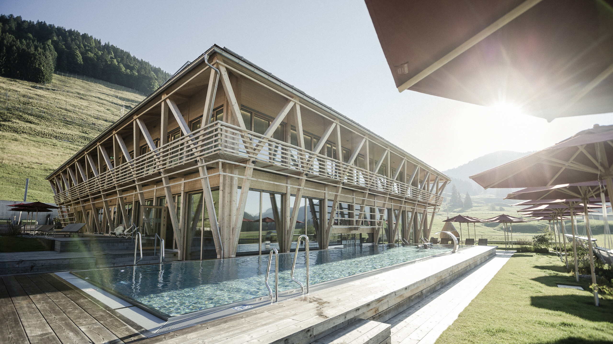 Infinity-Pool des Wellnesshotel HUBERTUS Mountain Refugio Allgäu im Sonnenlicht